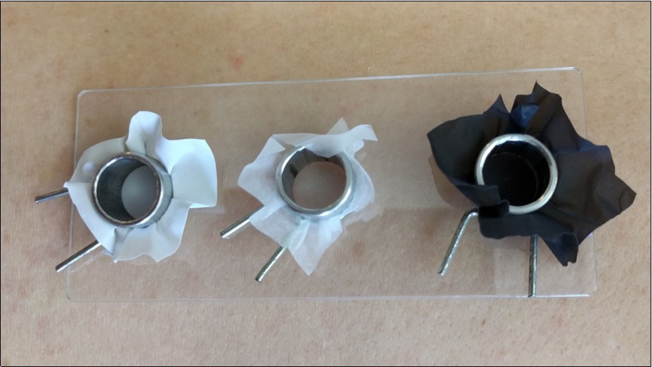 The “open chamber” test device. 1 mm thick transparent and flexible acrylic support with three circular spaces for fitting in three circular chambers made of chemical-resistant stainless-steel. Rectangular pieces of glove were fixed with a nickel-free metallic clip to the chambers, thus constituting the bottom of the chamber. The chambers were filled with the oxidative hair dyes.